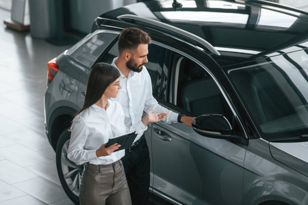 Assistant is helping the customer. Man with woman in white clothes are in the car dealership...