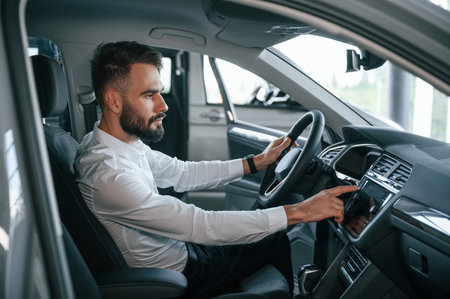 Examining the salon of the automobile. Young man in white clothes is in the car dealership.