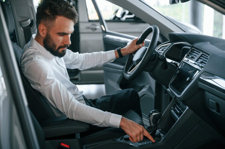 Examining the salon of the automobile. Young man in white clothes is in the car dealership.