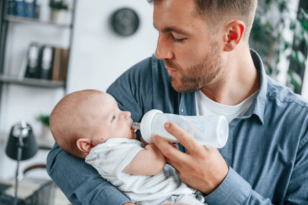 Feeding a baby. Father with toddler is indoors in the office.