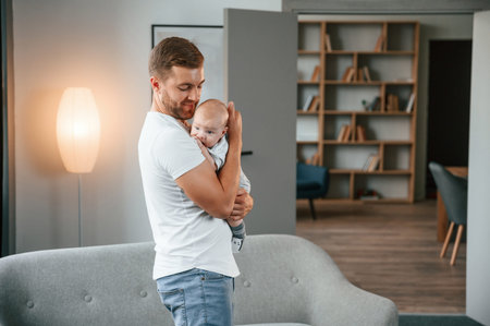 Standing with baby in hands. Father with toddler is at home, taking care of his son.