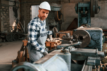 Side view. Operating the machine. Factory male worker in uniform is indoors.