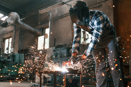 Welding of the iron. Factory male worker in uniform is indoors.