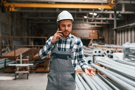 Talking by phone. Factory male worker in uniform is indoors.