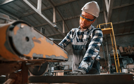 Handyman is working with factory machine. Warehouse employee in uniform is indoors.