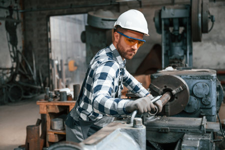 Manipulating the industry machine. Factory male worker in uniform is indoors.