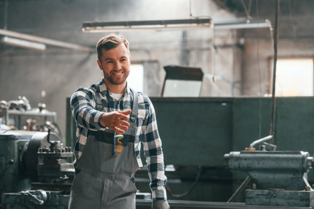 Friendly factory male worker in uniform is indoors giving hand.