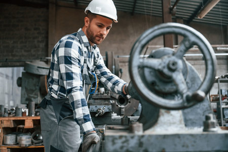 Factory male worker in uniform is indoors. With industry machine.