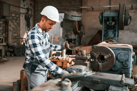 Side view. Operating the machine. Factory male worker in uniform is indoors.