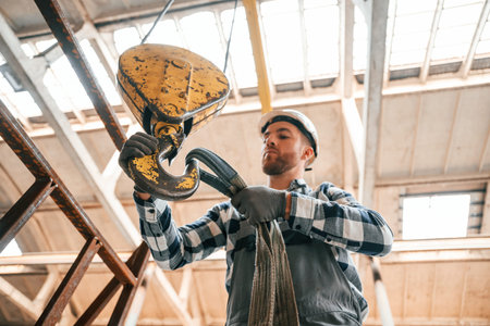 Working with crane. Man in a factory in uniform is indoors.