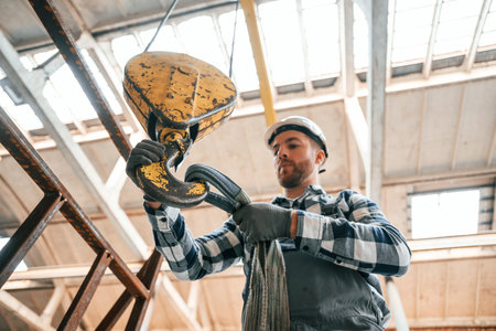 Working with crane. Man in a factory in uniform is indoors.