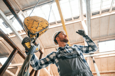 Working with crane. Man in a factory in uniform is indoors.