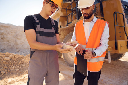 Checking rock that is in the hands. Two men in uniform are working together in the quarry.