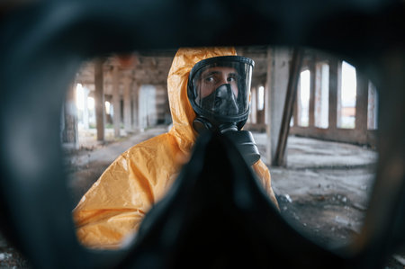 First person view through respirator. Man dressed in chemical protection suit in the ruins of the...
