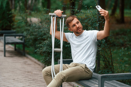 Man with crutches is in the park outdoors. Having leg injury.