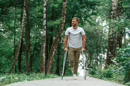 Enjoying the nature. Man with crutches is in the park outdoors. Having leg injury.