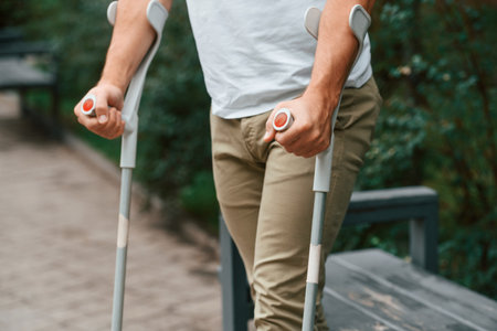 Close up view. Man with crutches is in the park outdoors. Having leg injury.の写真素材