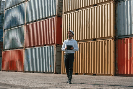 Walking and holding tablet. Male worker is on the location with containers.の写真素材