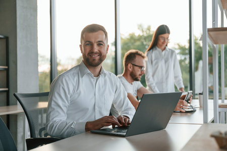 Sitting by laptop. Three people in formal clothes are working in the modern office together.