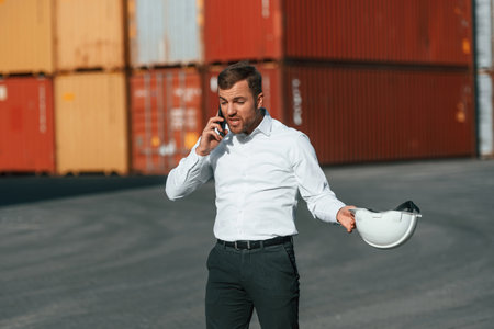 Angry, talking by phone. Male worker is on the location with containers.の写真素材