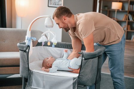 Newborn baby is in the cradle. Father is indoors. Conception of single dad.の写真素材