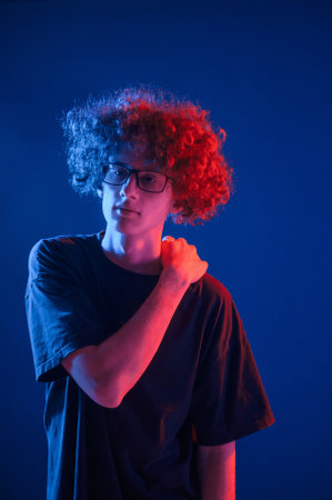 Posing for the camera. Young man with curly hair is indoors illuminated by neon lighting.の写真素材