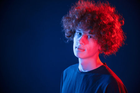 Portrait of young man with curly hair that is standing indoors, illuminated by neon lighting.の写真素材