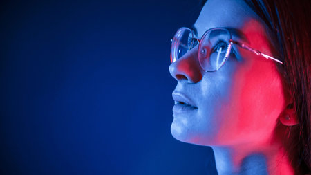 In glasses. Close up view. Young beautiful woman is indoors in the studio illuminated by neon light.の写真素材