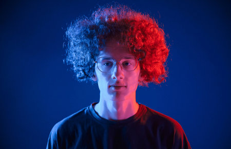Serious facial expression. Young man with curly hair is indoors illuminated by neon lighting.の写真素材