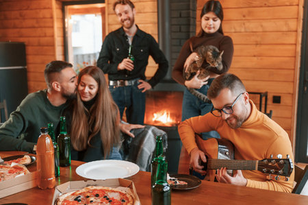 Sitting by the table with pizza and beer. Group of friends is having good weekend indoors.の写真素材