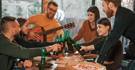 Man is playing guitar. Group of friends is having good weekend indoors in the wooden building together.の写真素材