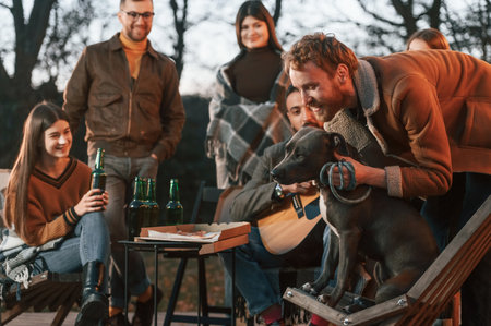 Man is petting his dog. Group of people is spending time together on the backyard at evening time.の写真素材