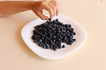the child takes a berry of a bilberry which lie on a white plateの写真素材