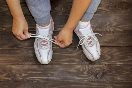 Tying Shoe laces girl sitting on the wooden floor. White sneakers on a dark wooden background.The view from the top.の写真素材