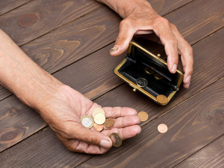An elderly person holds the coins over the old empty wallet. The concept of poverty in retirement. 