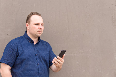 Young man uses his smart phone leaning against a concrete  wall. Man reading a message on mobile phone with copyspace.の写真素材