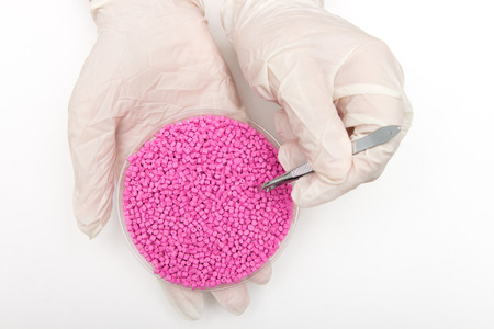 Plastic pellets . Colorant for polymers in granules. Worker wearing gloves takes plastic pellets with tweezers.の写真素材