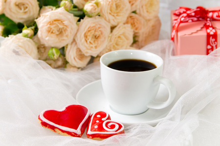 Wedding background . Valentine's day background . Cup of coffee and a lot of roses ,Gingerbread Heart  on a background of white organzaの写真素材