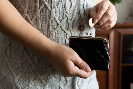 The woman holds the coins over the old empty wallet. The concept of poverty 