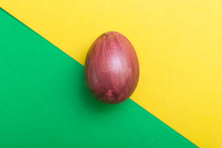 Easter Eggs on green and yellow geometric background. Burgundy egg handmade new style of colouring on a colored cardboard. Pattern, easter concept.Flat, top view of egg, geometric background.の写真素材
