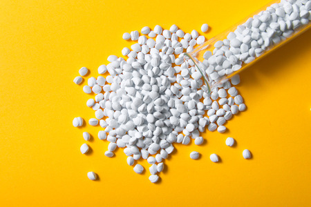 Plastic pellets. White Colorant for plastics, in test-tube against a yellow background. Plastic Raw material .の写真素材