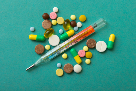 A thermometer with a color pills on turquoise background with copy space.The mercury thermometer to measure the temperature of the human body.の写真素材