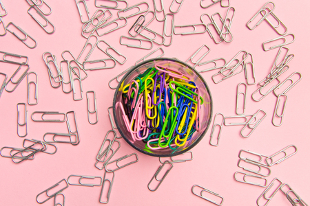 The concept of order and chaos. Chaotic scattered silvery paper clips on pink background and ordered stacked multicolored paper clips. The concept of organized societyの写真素材