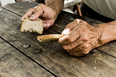 Hands the poor old man's, piece of bread and change, pennies on wood background. The concept of hunger or poverty. Selective focus. Poverty in retirement.Homeless.の写真素材