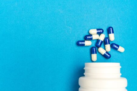 capsules ,pills  were poured from a white bottle on a blue background. の写真素材