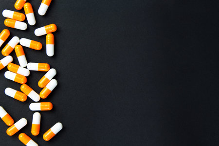Capsules (pills) orange and white were posted in the black background. Medical background, template.