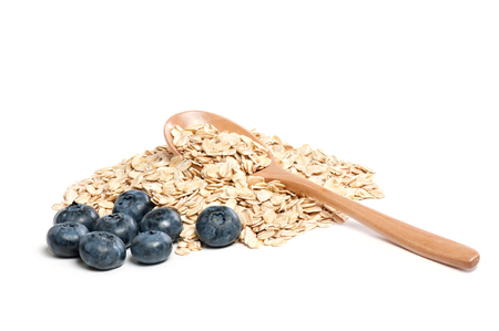 Pile of raw oatmeal flakes with the wooden spoon with fresh blueberries isolated on white.の写真素材