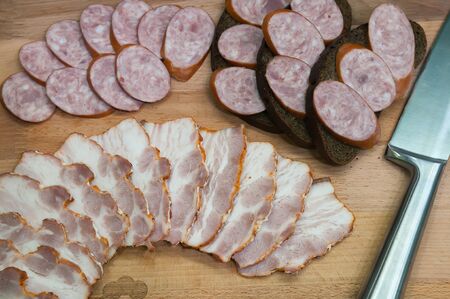 Rye bread sandwiches with smoked sausage and sliced bacon on wooden board. Rustic meat buffet top view.の写真素材