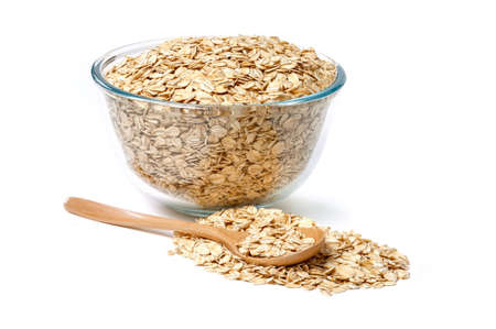 Oat flakes in glass bowl and wooden spoon isolated on white background.の写真素材