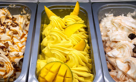Mango ice cream with fruit pieces top view. Various ice creams in trays in the ice cream shop.の写真素材